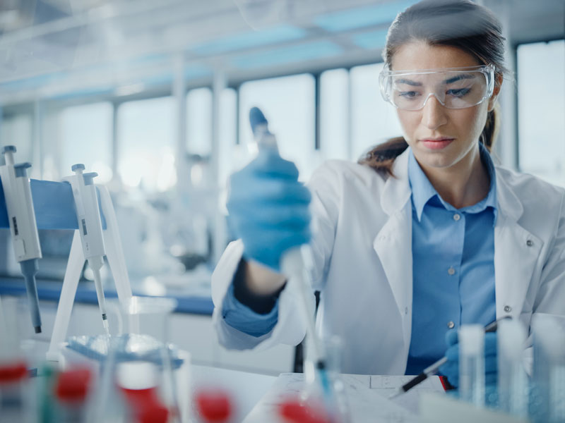 Woman in lab filling a beaker with liquid in a syringe